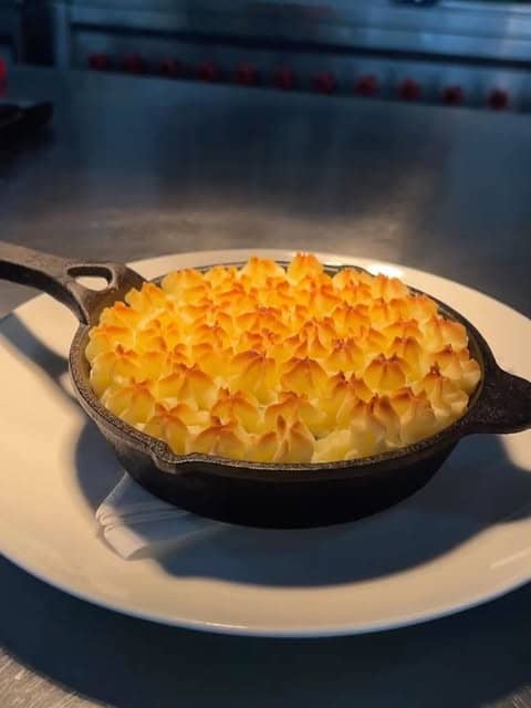 Fisherman's pie with a piped potato top in a cast iron pan, a dish in development in the open kitchen