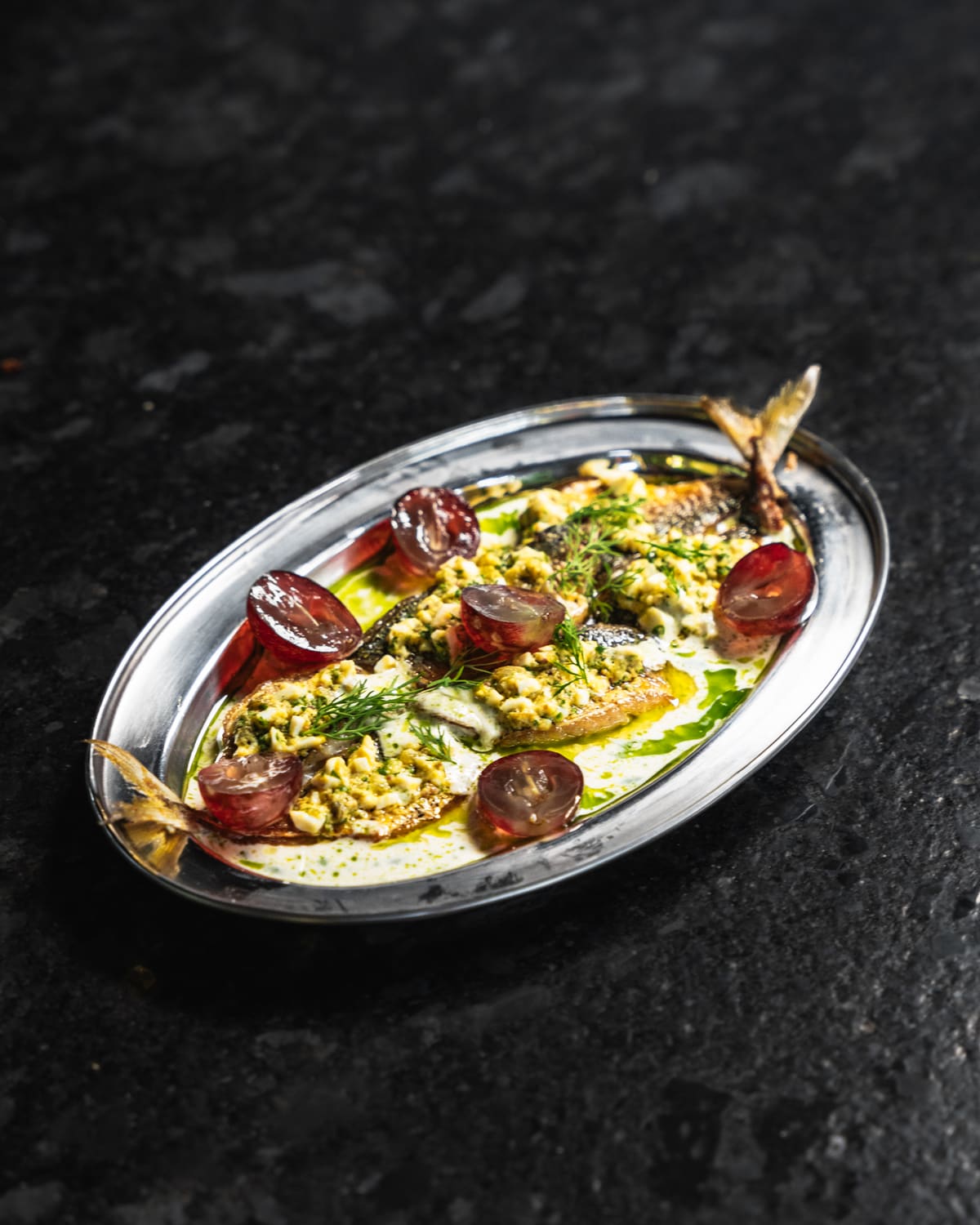 Charred tomatoes with a green herb crumb on a steel oval plate